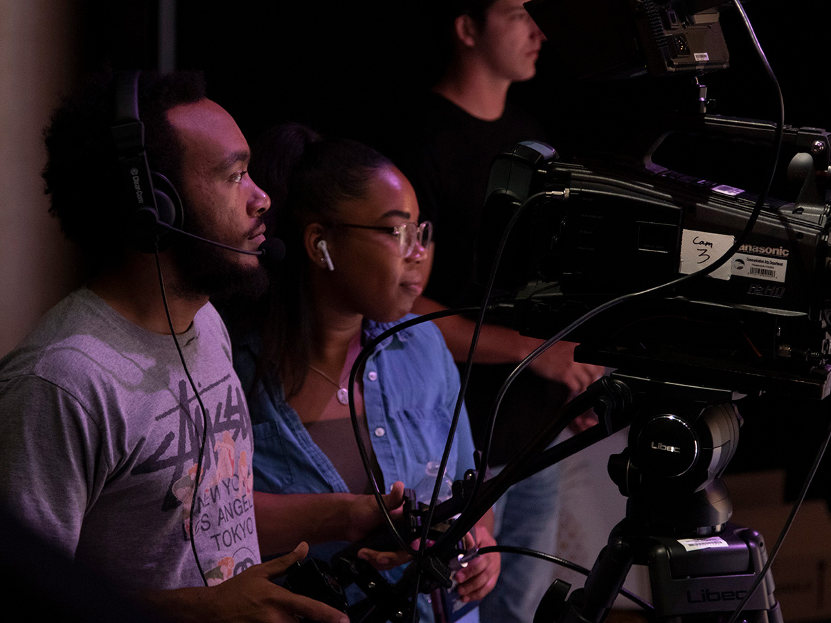 An instructor for Georgia Southern's B.S. in Multimedia and Film Production program helps a student learn to use a camera with headset on.