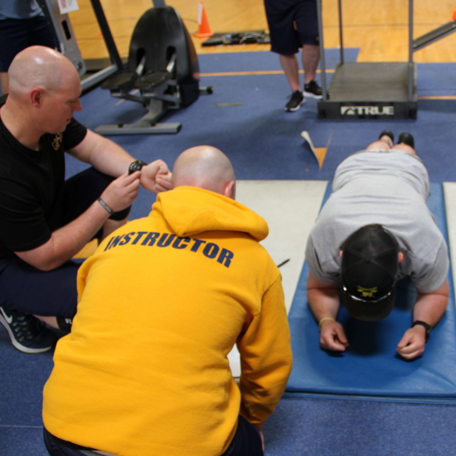An instructor conducts a physical plank test with students for hands on field training in health and kinesiology.