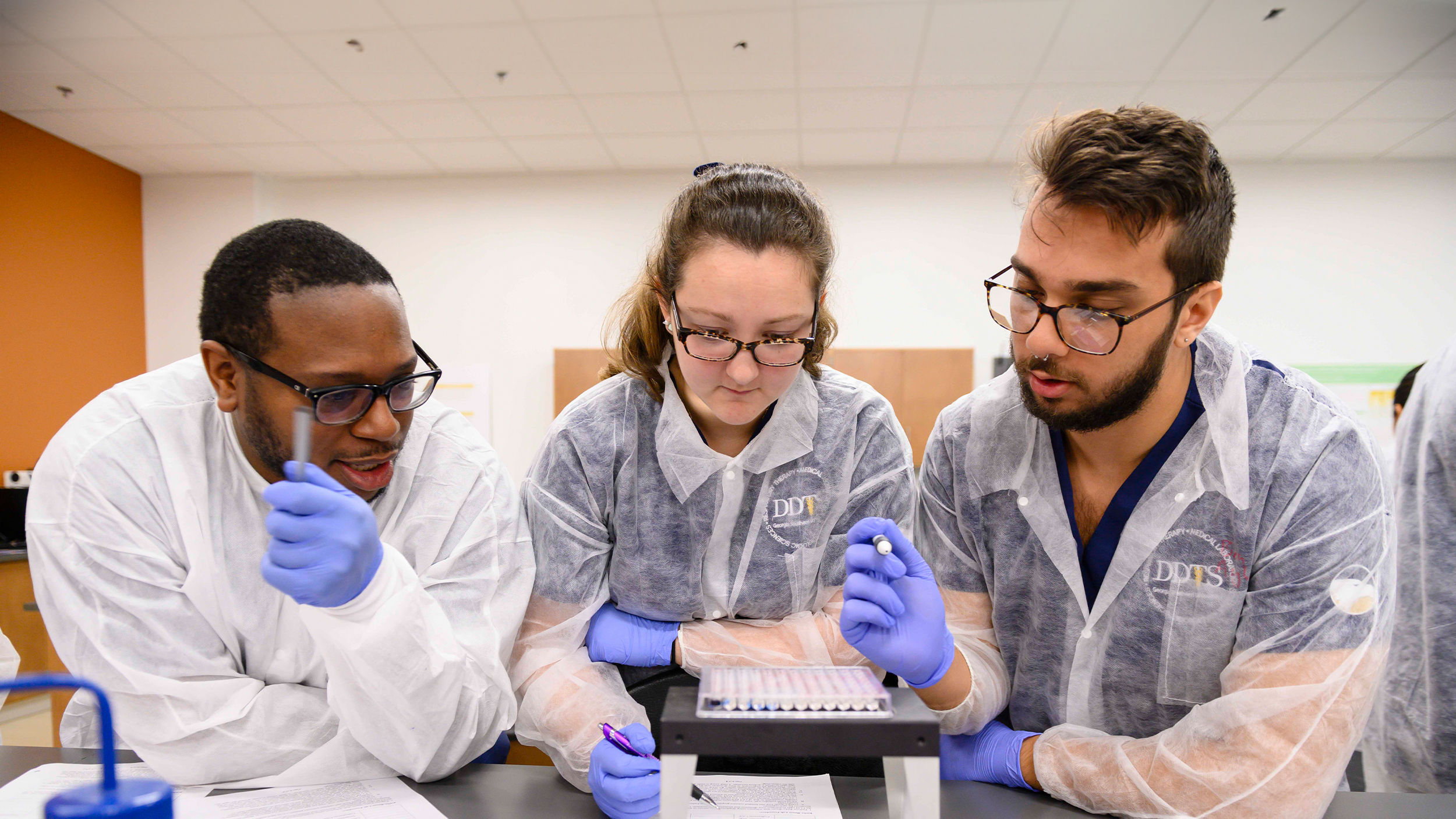 Three Georgia Southern students in lab coats conduct tests at the Waters College of Health Professions.