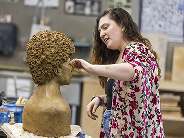 A Georgia Southern Department of Art student sculpts a bust out of clay in an art studio