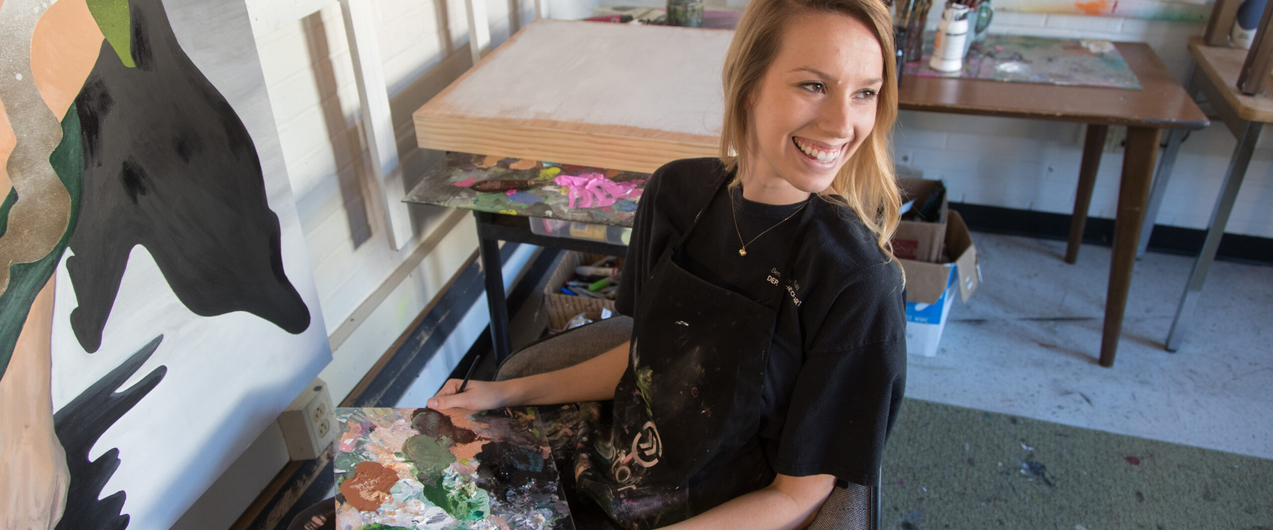 georgia southern student at art desk with paint, continuing work on fine art project