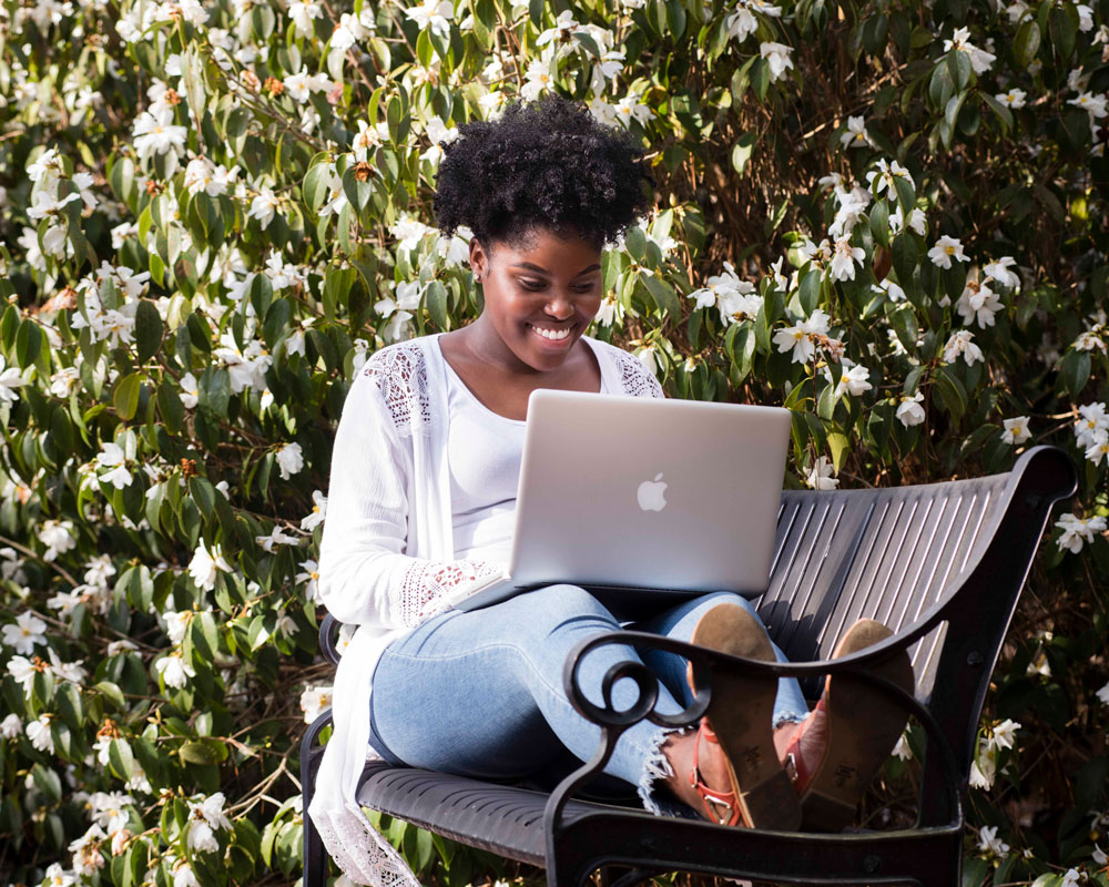 A Georgia Southern student works from a park bench outside while earning a degree online.