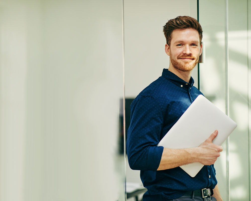 Smiling young man standing with laptop.