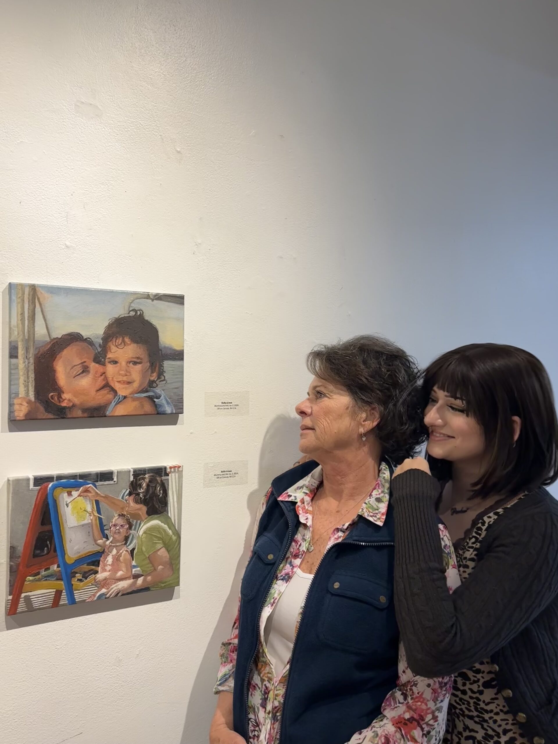 Bella Urzua (right) and her mother look at artwork created by Urzua. The pieces are painted translations of family photos.