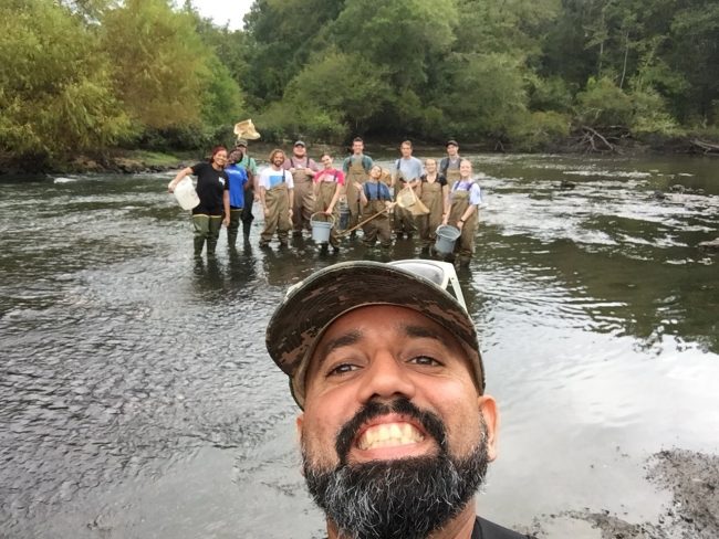 Biology professor Checo Colón-Gaud, Ph.D., stands and poses with his students in a river.