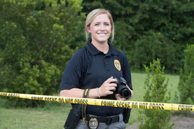 A law enforcement officer holds a camera at a crime scene.
