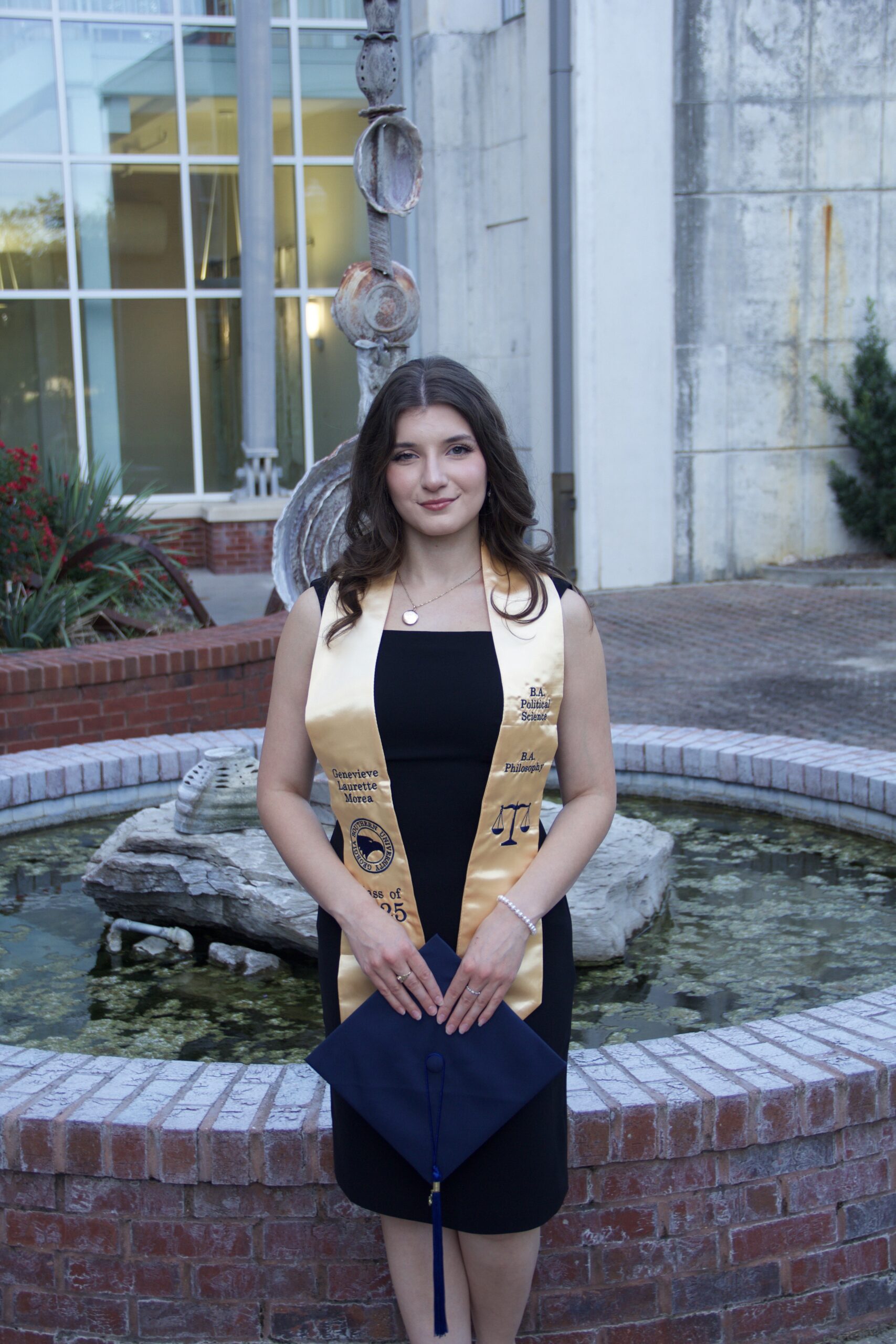 A college graduate stands next to a fountain