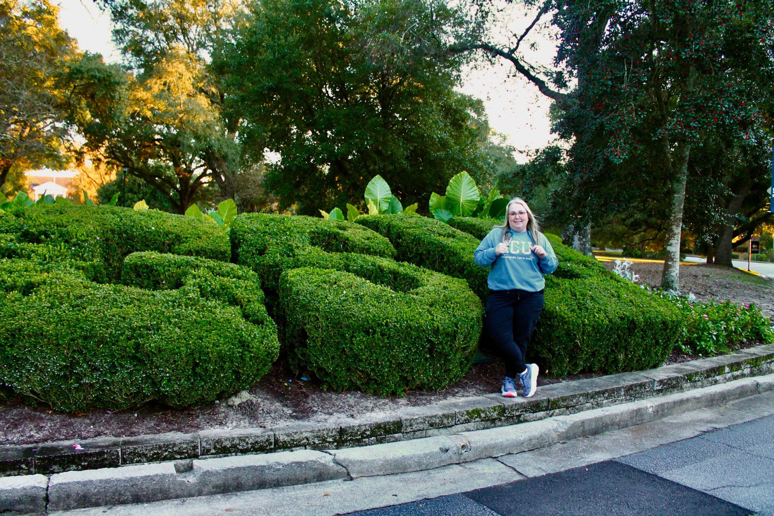 Melissa Miles is wearing an ICU Nurse sweatshirt and a stethoscope while standing in front of the GSU bushes on Sweetheart Circle at Georgia Southern University.